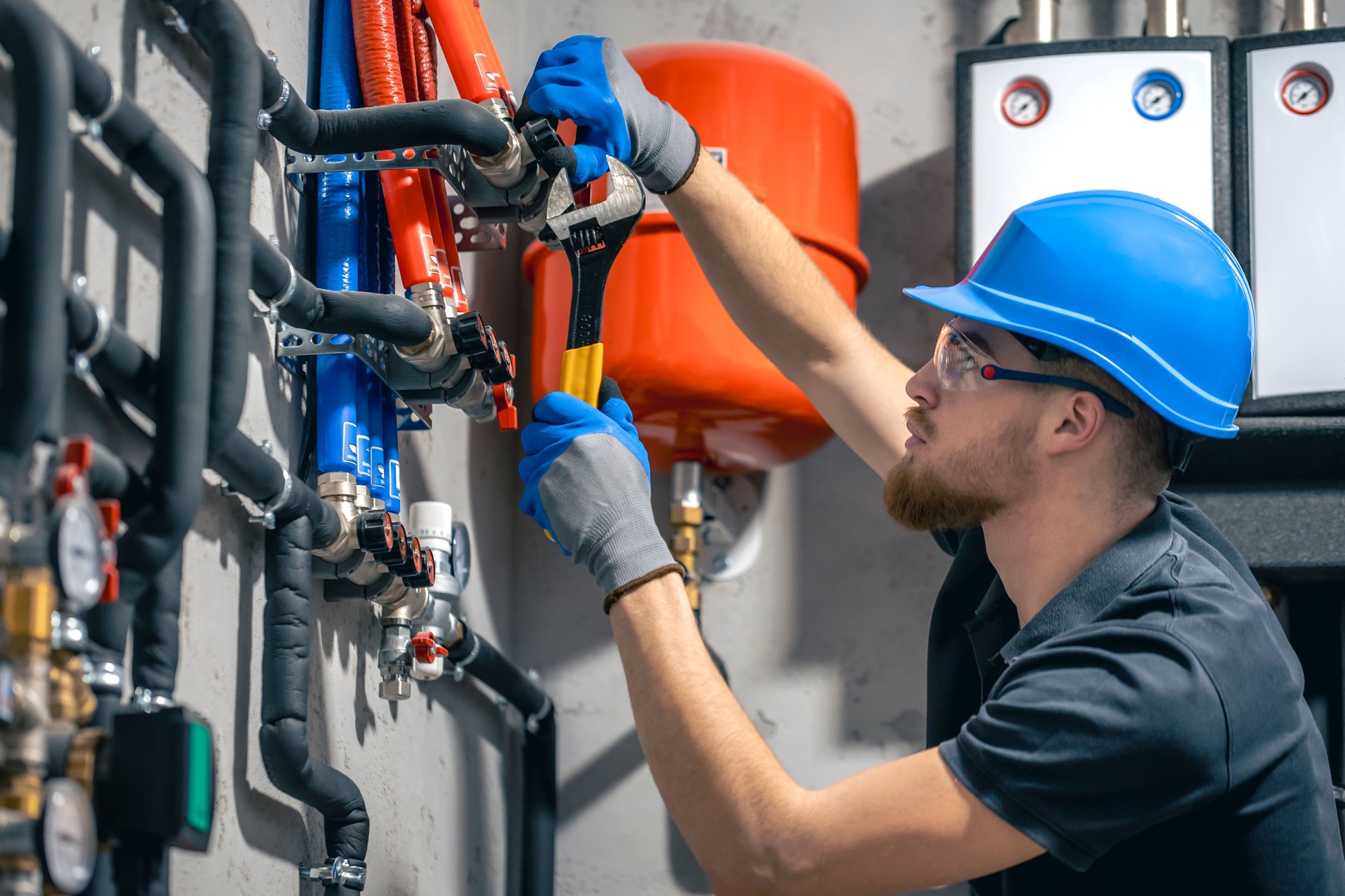 A man installs a heating system in a house and checks the pipes with a wrench.